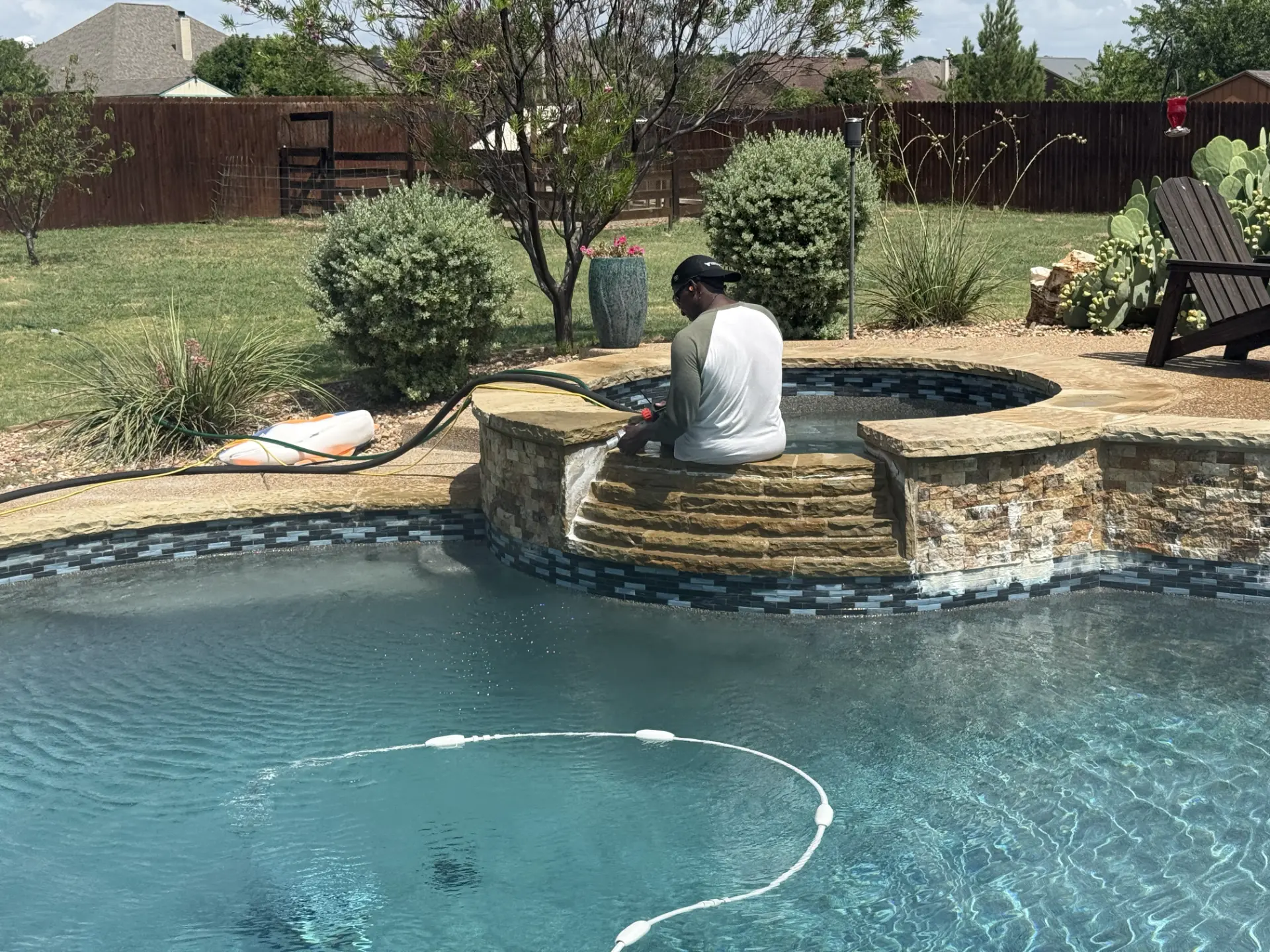 Technician cleaning calcium from a pool spa wall in a Texas backyard