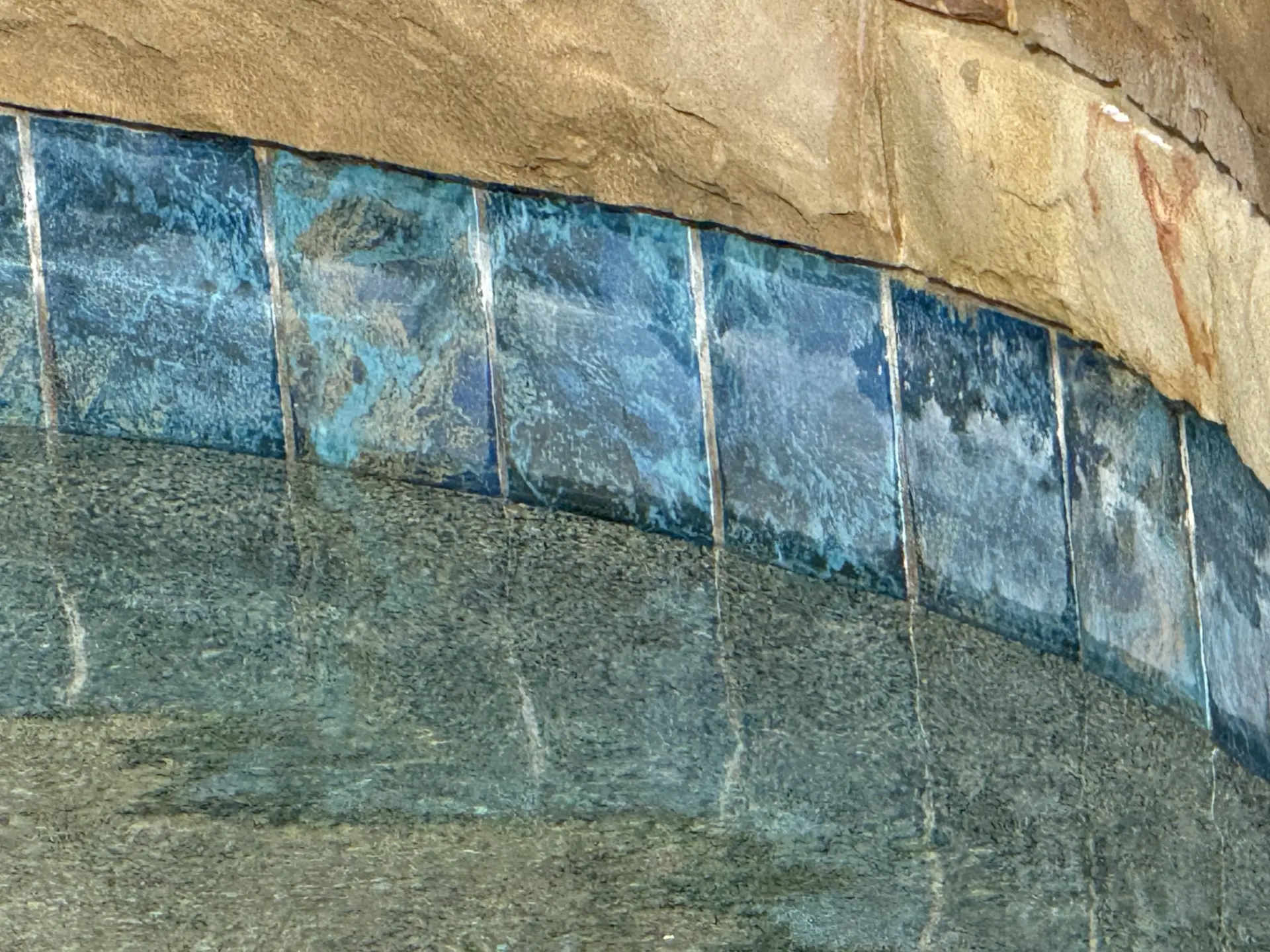 Blue waterline tile with heavy calcium scale beneath stone coping